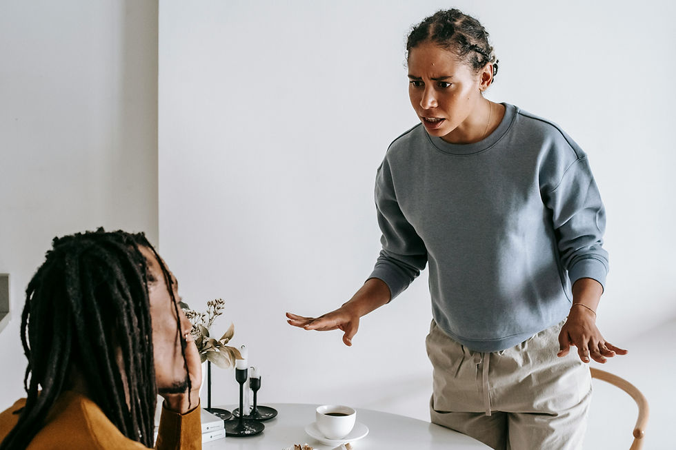 Two people in a heated discussion at a table with a cup, books, and candles. One is standing, gesturing, looking upset. Plain background.