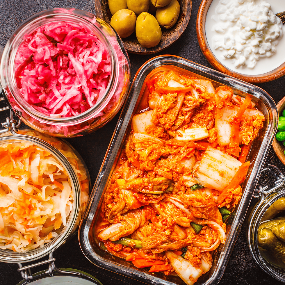 Jars of colorful pickled vegetables and kimchi on a dark surface. Olives and cottage cheese in bowls add contrast to the vibrant scene.