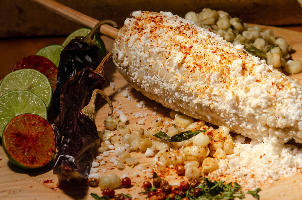 Mexican street corn coated in cheese and chili, with limes and dried chiles on a wooden board.