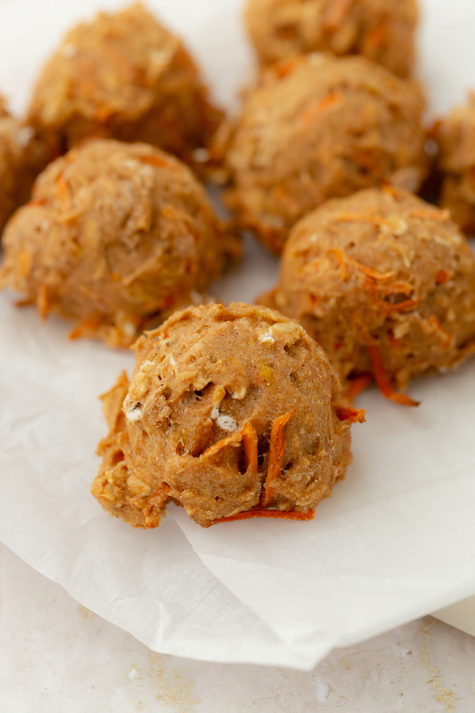 Close-up of several round, brown dog cookies with visible carrot shreds on white parchment paper. Soft texture and warm, earthy colors.