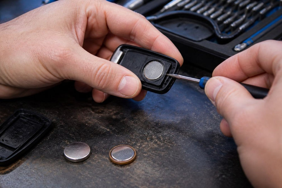 Hands using a flathead screwdriver to open a car key fob to replace its old coin-cell battery
