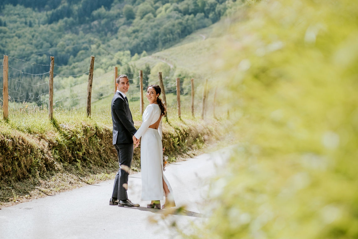 Novios caminando de la mano en un entorno natural rodeado de montañas y campos verdes durante una boda en Bizkaia."