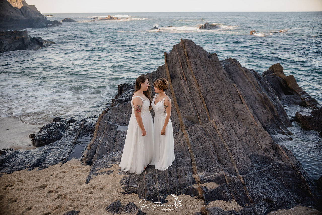 Pareja de recién casadas posando en las rocas con el mar de fondo en Saturraran