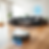 Robot vacuum on wooden floor in a modern living room with a gray sofa. A glowing blue icon of a person on the wall indicates smart tech.