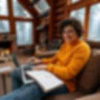 Smiling person in a yellow sweater uses a laptop in a cozy log cabin with a lit fireplace. Foggy forest visible through large windows.