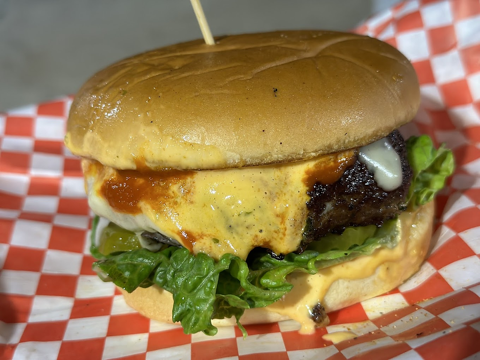 Cheeseburger with lettuce, grilled patty, and melted cheese on a bun, topped with sauce. Served on a red and white checkered paper.