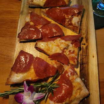 Slices of pepperoni pizza on a wooden board, garnished with rosemary and a purple flower, set on a dark table.