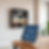 Tablet on a stand displaying app icons in a modern room with wooden shelves and plants. Warm lighting creates a calm atmosphere.
