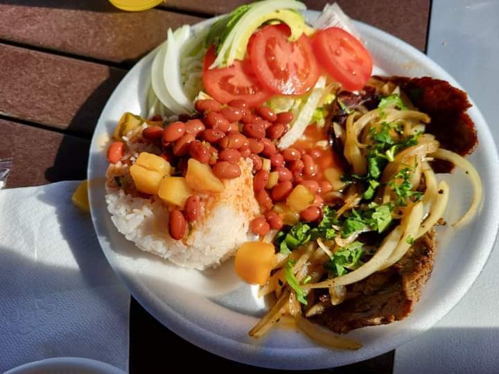 Plate of rice, red beans, diced vegetables, onions, and beef topped with cilantro and sliced tomatoes on a sunny table.