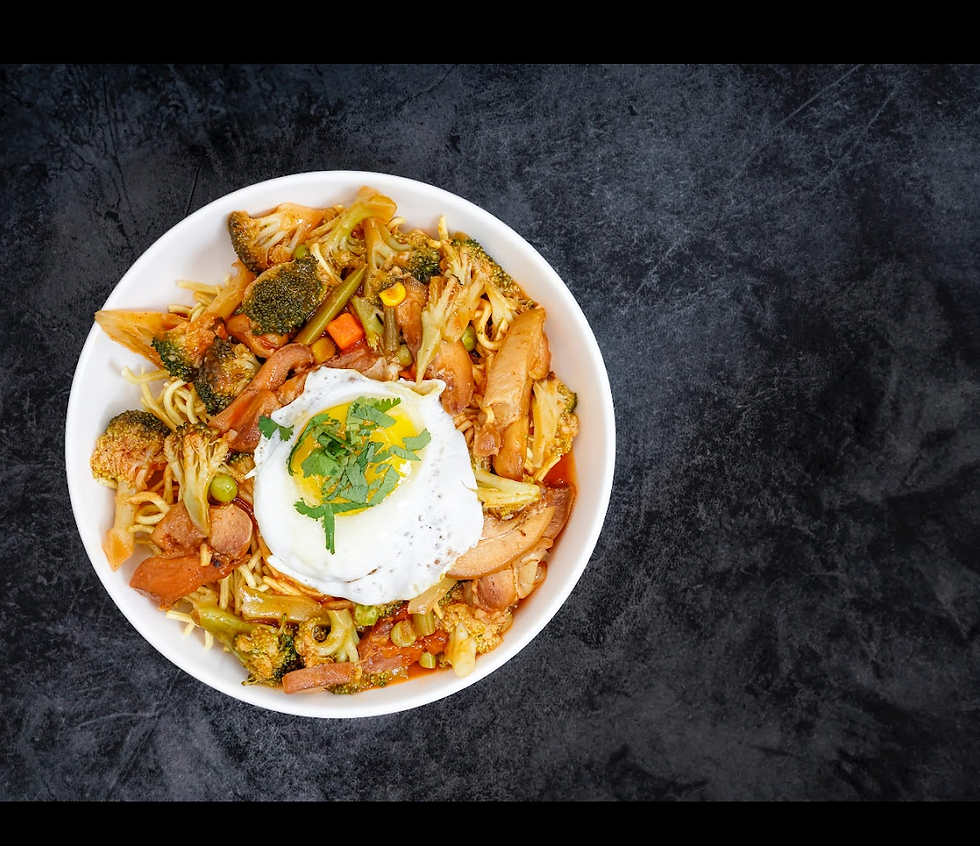 Bowl of stir-fry with noodles, broccoli, and vegetables topped with a fried egg and herbs. Dark textured background. Bright and appetizing.