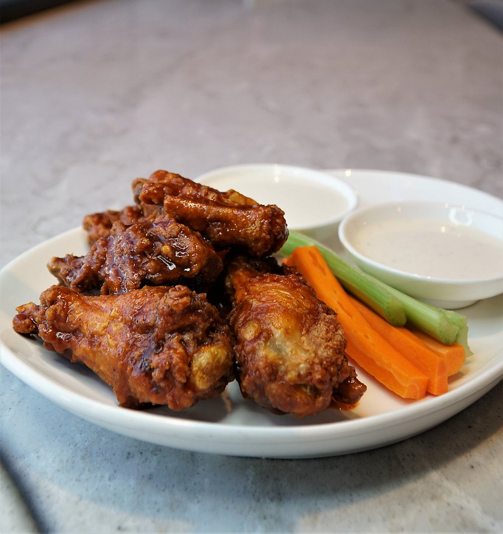 Chicken wings with a crispy texture on a plate, served with carrot and celery sticks, and two white dipping sauces on a gray table.
