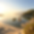 Three people kayak on a calm lake at sunrise, surrounded by sandy dunes and tall grass. The water is serene, reflecting pastel skies.