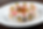 Sushi rolls topped with pink fish slices, garnished with green onions, encircle a dish of sauce on a white plate; sprinkled spices.