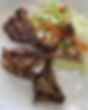 Grilled lamb chops on a white plate with a fresh salad mix of lettuce, diced tomatoes, and greens. The dish appears appetizing and colorful.