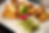 A plate with spring rolls, chicken wings, green dumplings, a radish, lemon wedge, and mint leaf garnish, on a white background.