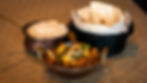 Copper bowls with rice and vegetable curry on a textured table. A black basket with bread nearby. Warm, inviting colors.