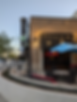 Bar Louie entrance with patio seating, string lights, a blue umbrella, and a neon martini sign. Evening atmosphere with a relaxed vibe.
