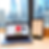 Laptop displaying clothing site on desk by window with cityscape view. Framed sales tax certificate and candles beside it. Bright daylight.