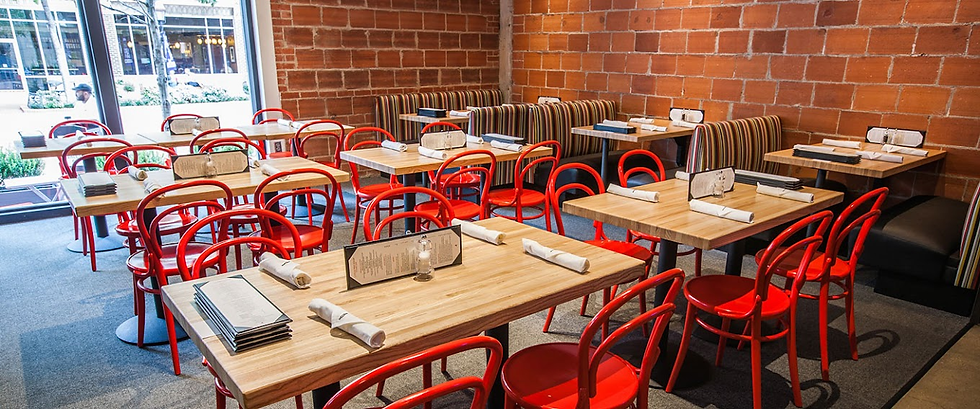 Empty restaurant with wooden tables and red chairs. Brick walls and striped booth seating create a modern, cozy ambiance. Menus on tables.