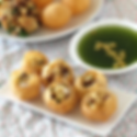 Plate of filled pani puri on a floral tablecloth, accompanied by a bowl of green water and chickpeas, with a side of mixed chaat.