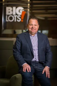 Professional portrait of a person seated indoors with a Big Lots sign in the background.