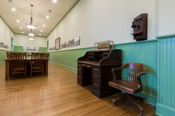 Renovated commercial interior with wood flooring, historic desk, vintage wall telephone, green wainscoting, and display photographs.