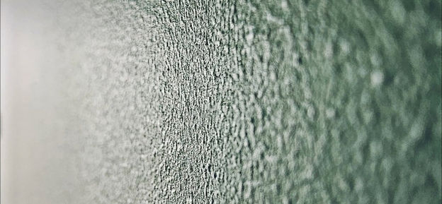 Detal ściany wykończonej farbą w kolorze butelkowej zieleni o idealnej, jednolitej strukturze.