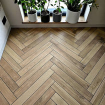 Podłoga wyłożona płytkami drewnopodobnymi w jodełkę francuską na parterze przy oknie z parapetem i zielonymi roślinami doniczkowymi.