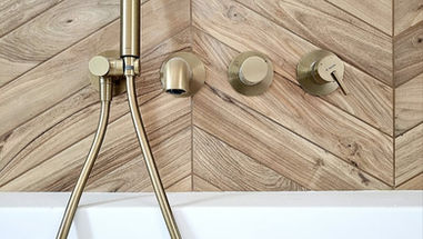 Złota armatura podtynkowa Deante zamontowana na tle płytek drewnopodobnych ułożonych w jodełkę klasyczną.