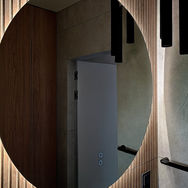 Duże, okrągłe lustro łazienkowe z podświetleniem LED, drewniane lamele na ścianie, nowoczesne czarne lampy wiszące, industrialny styl.