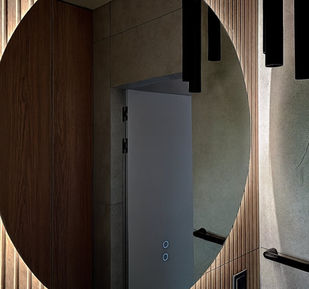 Owalne lustro z obwodowym podświetleniem LED wkomponowane w pionową okładzinę ścienną.