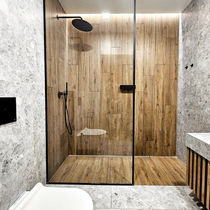 Widok na nowoczesną łazienkę z szarym marmurem, białą podwieszaną toaletą i przeszkloną kabiną prysznicową z drewnopodobnymi płytkami.