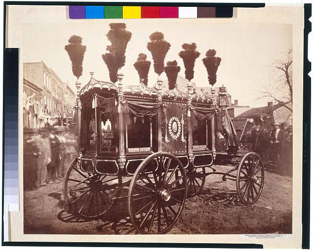 Ornate horse-drawn hearse with plumed top, set in a blurry street scene. Intricate designs and dark drapery on a sepia-toned background.