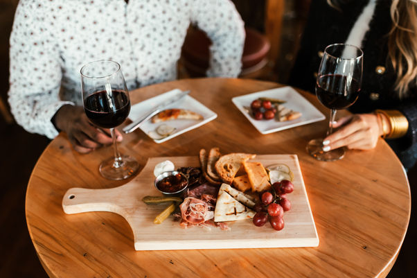 Wine glasses and charcuterie board on a wooden table with assorted food.