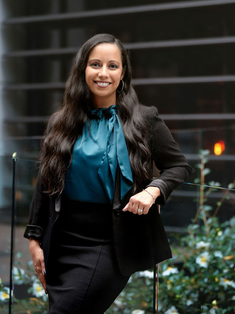 Smiling woman wearing a blue shirt and black blazer poses outside a building.