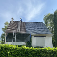 Toiture en cours de rénovation à Marcoussis, partiellement nettoyée, avec un couvreur travaillant au sommet et une échelle posée sur le toit.