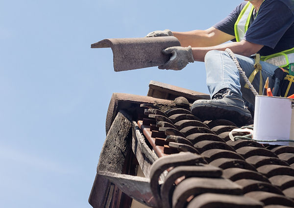 Couvreur en train de poser une tuile sur un toit, équipé de gants et harnais de sécurité, sous un ciel bleu.