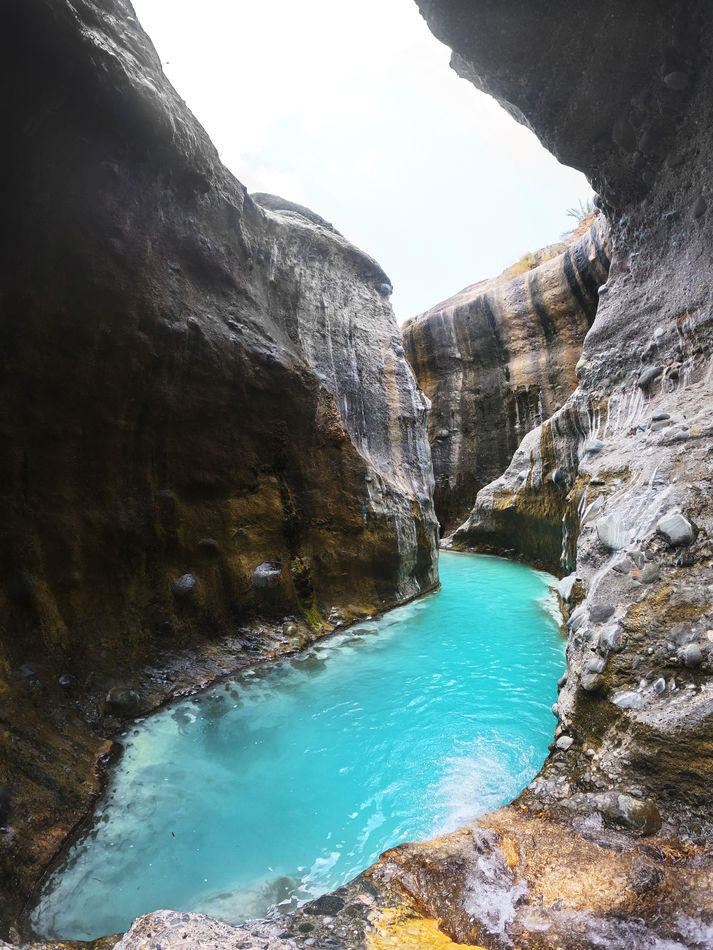 Bright turquoise canyon pool between steep rock walls on the Wadi Hoqain hiking route