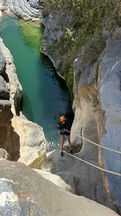 Canyoner descending above a turquoise pool on the Wadi Nakhr guided canyoning tour
