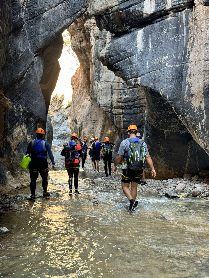 Adventure group walking through shallow water inside Snake Canyon during a guided canyoning trip in Oman