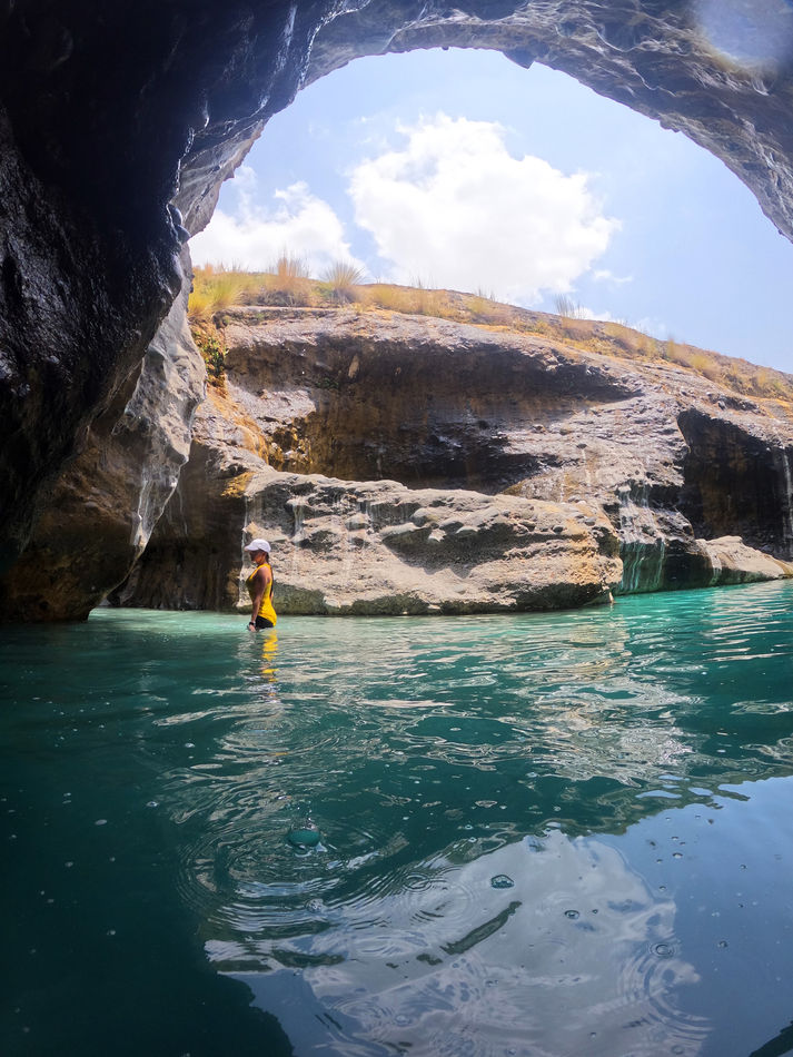 Scenic swimming pool framed by a rocky arch in Wadi Hoqain, Oman