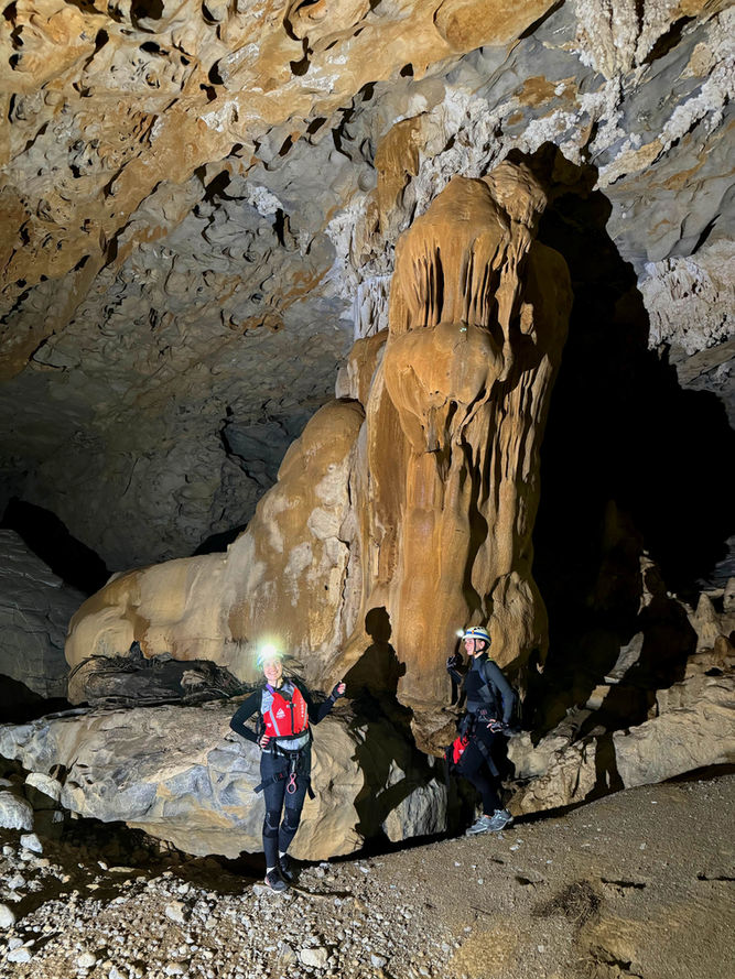 Visitors standing beside a giant stalagmite during the Al Hoota Cave caving experience in Oman