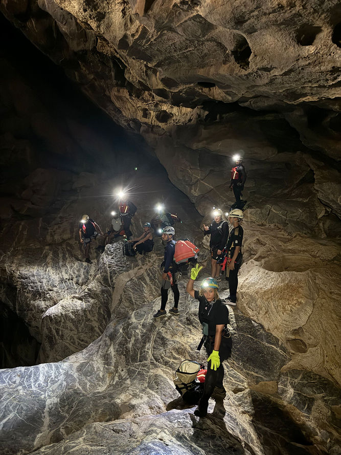 Caving group exploring a large underground chamber on the Al Hoota Cave Crossing adventure