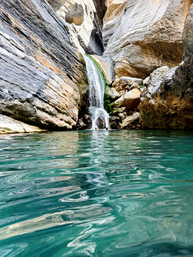 Emerald canyon pool with a small waterfall in Wadi Sa’ada during a one-day hike in Oman