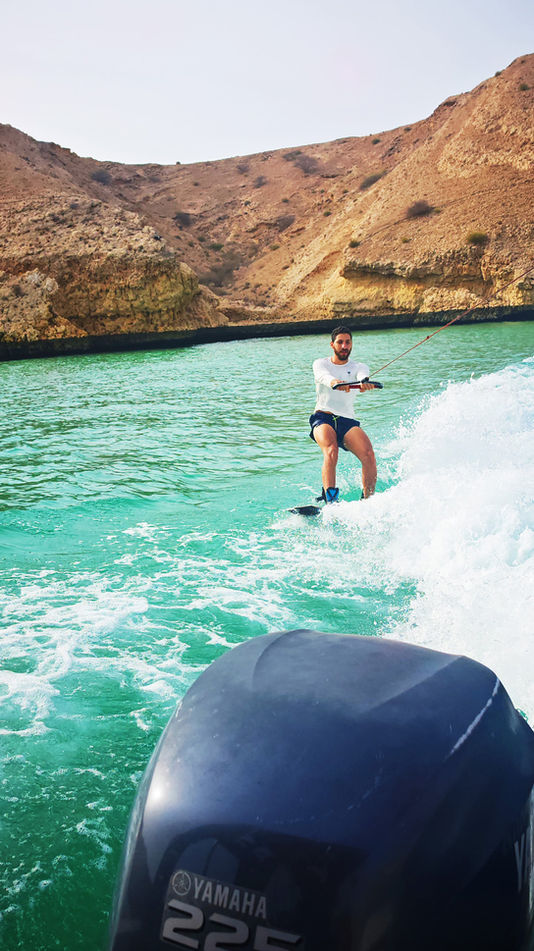 Wakeboarder riding across turquoise water on a Qantab Islands boat tour near Muscat, Oman