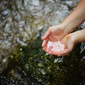 Zwei Hände die eine Schale bilden und Wasser aus einem Bach schöpfen.