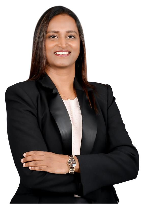 A woman in a black blazer and watch smiles confidently with arms crossed against a white background.