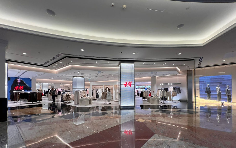H&M store interior with clothes displayed. Shiny marble floor reflects the ceiling lights. Large H&M logo sign is visible, creating a stylish and modern vibe.