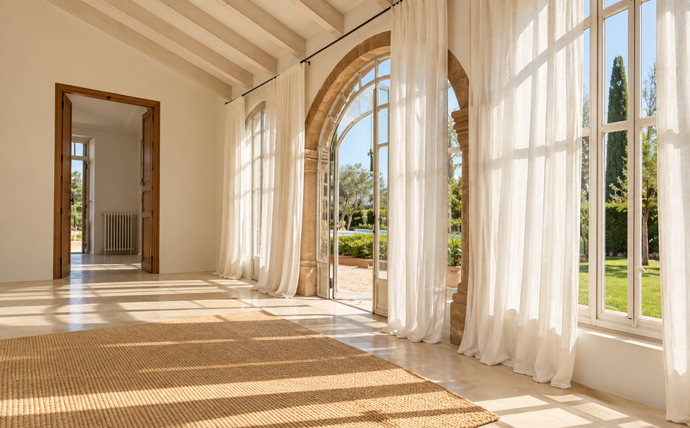 Galería de vivienda mediterránea con ventanales en arco, cortinas de lino blanco y suelo de barro cocido