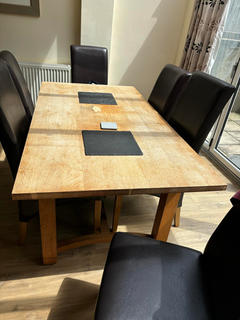 Rectangular wooden dining table with six black leather chairs. The table has a light-colored wood top and a darker base.